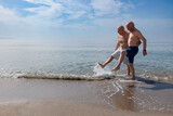 Fototapeta  - coppia di anziani al mare giocano sula riva schizzando e calciando l''acqua