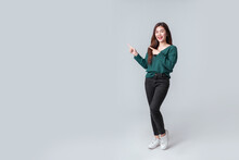 Full Length Asian Woman In Casual Green Sweater Pointing To Empty Space On Isolated Grey Background. Happy Anniversary Or New Year Festival Concept.