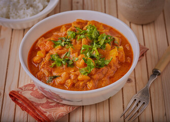 Wall Mural - Thai styled prawn curry garnished with herbs on a wooden table.