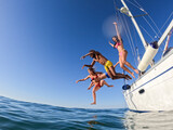 Group of friends diving in the water during a sailboat excursion, young people jumping inside ocean in summer vacation from a sail, having fun, luxury vacation lifestyle