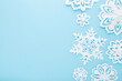 © fotoduets - Different white snowflake shapes created from paper on light blue table background. Pastel color. Closeup. Top down view. Handmade decoration elements for winter festive. Empty place for text.