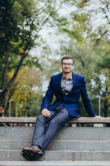 A man in a suit is sitting on a bench in the park