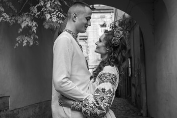 Wall Mural - Black and white portrait. A happy young couple in love, a family walking through the old city of Lviv in Ukrainian embroidered dresses, holding hands. Young people hug in the old town of Lviv