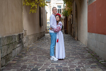 Wall Mural - A happy young couple in love, a family walking through the old city of Lviv in Ukrainian embroidered dresses, holding hands. Young people hug in the old town of Lviv
