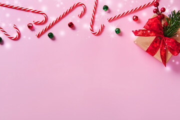 Wall Mural - Christmas composition. Border made of candy canes and gift box, holiday decorations on a pink background.