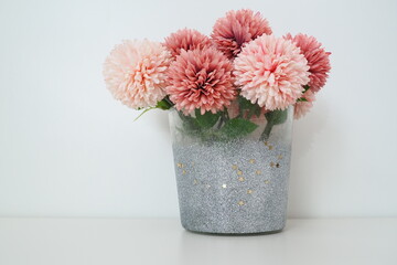 Bouquet of pink terry artificial flowers in a gray silver vase on a white background. Still life, interior decoration option. Room decor. Free space for text.