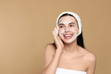 Wall Mural - Happy young woman washing face with cosmetic product on beige background, space for text
