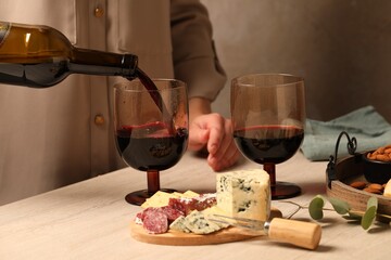 Canvas Print - Woman pouring red wine into glass at wooden table, closeup