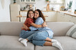 © DimaBerlin - Carefree happy family of millennial woman and teenage girl hugging sits on big sofa in living room. Positive cheerful daughter hugging mother after long separation or arrival from school camp