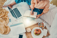 Marketing, laptop and woman writing with breakfast on her bed, working and planning information for strategy from above. Remote employee with business notes, food and report for creative work on a pc