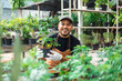Happy gardener man in gloves and apron plants flowers in greenhouse. Florists man working gardening in the backyard. Flower care harvesting. Planting in pot with dirt or soil