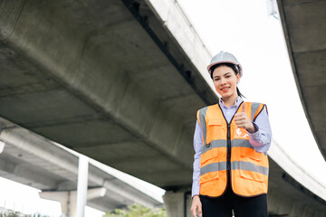 Wall Mural - Asian engineer worker woman or architect looking construction with white safety helmet in construction site. Standing at highway concrete road site. Progress planning of highway bridge.