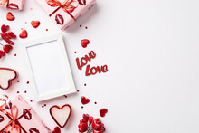 Valentine's Day Concept. Top View Photo Of Photo Frame Gift Boxes In Wrapping Paper With Kiss Lips Pattern Red Hearts Confetti Inscriptions Love Candles On Isolated White Background With Blank Space