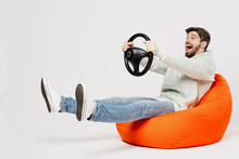 Full Body Excited Amazed Happy Young Caucasian Man Wear Mint Hoody Sit In Bag Chair Hold Steering Wheel Driving Car Isolated On Plain Solid White Background Studio Portrait. People Lifestyle Concept.