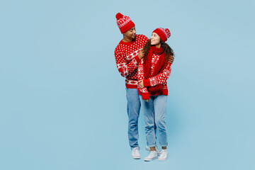 Wall Mural - Full body merry fun young couple two man woman wearing red Christmas sweater Santa hat posing hug look to each other isolated on plain pastel light blue background Happy New Year 2023 holiday concept.