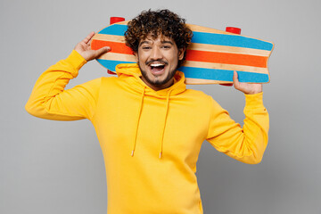Wall Mural - Young smiling happy fun cool cheerful Indian man 20s he wearing casual yellow hoody hold skateboard pennyboard look camera isolated on plain grey background studio portrait. People lifestyle portrait.