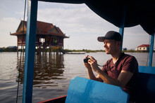 Portrait Of Tourist With Camera On Boat Floating On Lake. Floating Village On Tonle Sap Lake Near Siem Reap In Cambodia..