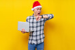 © Bangun Stock Photo - Worried young Asian man in plaid shirt wearing Christmas hat holding laptop pc computer and looking at watch, check time on yellow background. Christmas and Happy New Year 2023 holiday concept