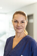 © wavebreak3 - Vertical portrait of smiling caucasian female healthcare worker in corridor, with copy space