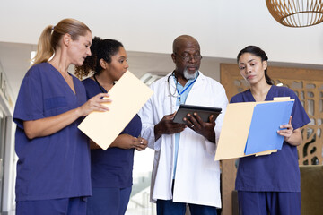 Wall Mural - Diverse group of healthcare workers with tablet and paperwork discussing in hospital corridor