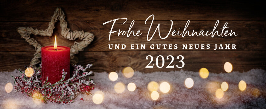 Fototapete - Greeting Card at Christmas and New Year 2023 with German text - Frohe Weihnachten und ein gutes neues Jahr 2023 - Red Candle, star and magic lights in snow before rustic wooden wall, Panorama, Banner