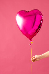 Sticker - Vertical of hand holding shiny pink heart shaped balloon on pink background with copy space