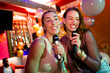 © Wavebreak Media - Two happy caucasian female friends singing karaoke at a nightclub bar