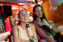 Two Happy Caucasian Female Friends Singing Karaoke At A Nightclub Bar