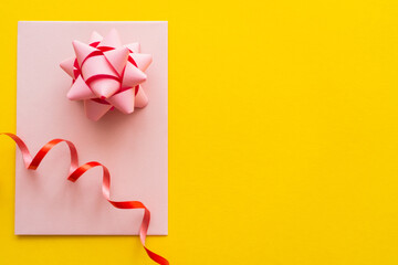 Wall Mural - top view of gift bow and serpentine on greeting card on yellow background.