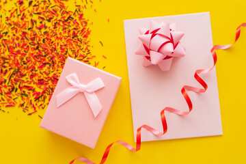 Wall Mural - top view of festive gift and greeting card near blurred sprinkles on yellow background.