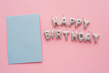 Wall Mural - Top view of greeting card near candles in shape of Happy Birthday lettering on pink background.