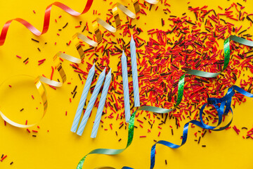 Wall Mural - Top view of festive candles near serpentine on sprinkles on yellow background.