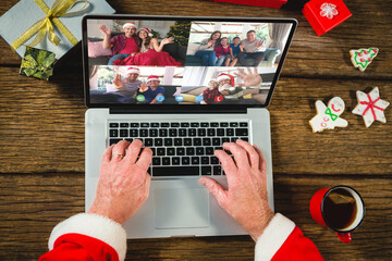 Wall Mural - Santa claus with christmas presents having video call with happy caucasian family