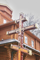 Wall Mural - A wooden cross with a crucifix near a wooden church.