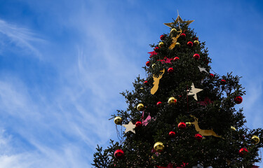 Outdoor Christmas tree with winter holidays decorations against blue sky landscape