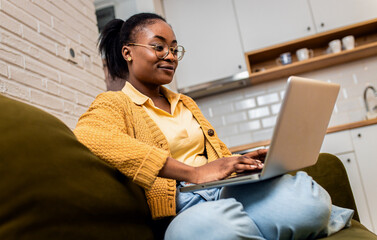 Wall Mural - Young African American female student studying at home using laptop.