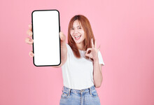 Asian Young Woman Showing Smart Phone With Blank Screen , White Screen For Mobile App Advertising Isolated On Pink Background ,Cell Phone Display Mock Up Image.