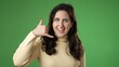 © Robert Peak - Portrait of smiling happy young woman 20s smiling and giving call me gesture with hands isolated on green screen background.