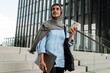 © Drobot Dean - Muslim woman holding laptop and smartphone while standing on stairs