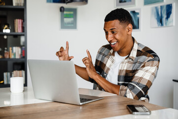 Canvas Print - Positive african man gesturing while having video call via laptop at home