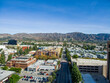 aerial shot of office buildings, apartments and shops surrounded by lush green trees, cars driving and parked on the street with majestic mountains and a clear blue sky in Burbank California USA