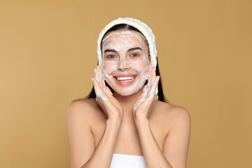 Wall Mural - Happy young woman washing face with cosmetic product on beige background