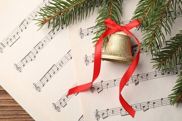 Wall Mural - Golden shiny bell with red bow, fir branches and music sheets on wooden table, flat lay. Christmas decoration