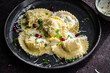 Mezzelune filled with parmesan and asparagus with creamy sauce decorated with parsley and pomegranate seeds on dark plate.