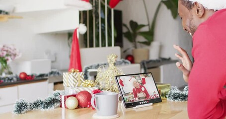 Wall Mural - African american man with santa hat having tablet video call with happy caucasian woman