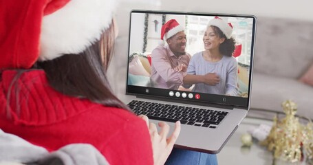 Canvas Print - Caucasian woman with santa hat having laptop video call with diverse couple