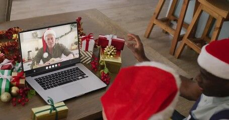 Canvas Print - Diverse couple with santa hats having laptop video call with caucasian man