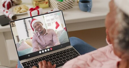 Wall Mural - Animation of african american woman in santa hat on laptop video call with man at christmas