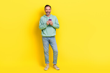 Full length photo of positive satisfied man use quality gadget stand empty space cool offer discount isolated on yellow color background