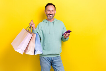 Wall Mural - Portrait of handsome optimistic man dressed green hoodie hand hold smartphone bags on shoulder isolated on yellow color background